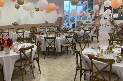 Salle décorée pour un événement, avec tables dressées, nappes noires, centres de table à plumes blanches et ballons dorés.