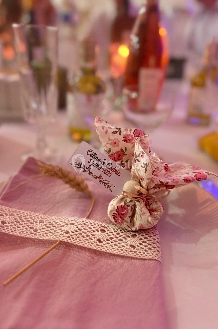 Serviette rose ornée de dentelle, épi de blé et sachet fleuri avec étiquette marquée ’Céline & Cédric, juin 2023’.