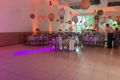 Salle décorée pour un événement, avec tables dressées, nappes noires, centres de table à plumes blanches et ballons dorés.