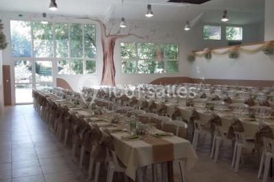 Salle décorée pour un événement, avec tables dressées, nappes noires, centres de table à plumes blanches et ballons dorés.