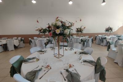 Salle décorée pour un événement, avec tables dressées, nappes noires, centres de table à plumes blanches et ballons dorés.
