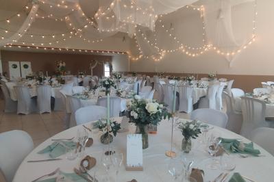 Salle décorée pour un événement, avec tables dressées, nappes noires, centres de table à plumes blanches et ballons dorés.