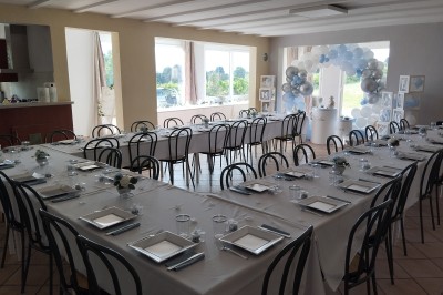 Salle décorée pour un événement, avec tables dressées, nappes noires, centres de table à plumes blanches et ballons dorés.