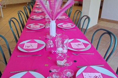 Salle décorée pour un événement, avec tables dressées, nappes noires, centres de table à plumes blanches et ballons dorés.