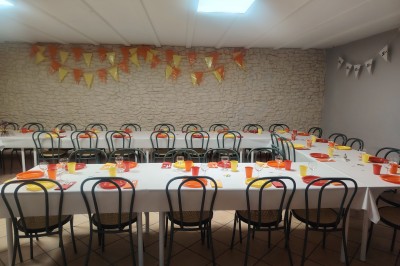 Salle décorée pour un événement, avec tables dressées, nappes noires, centres de table à plumes blanches et ballons dorés.