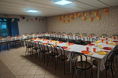 Salle décorée pour un événement, avec tables dressées, nappes noires, centres de table à plumes blanches et ballons dorés.