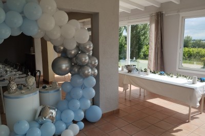 Salle décorée pour un événement, avec tables dressées, nappes noires, centres de table à plumes blanches et ballons dorés.