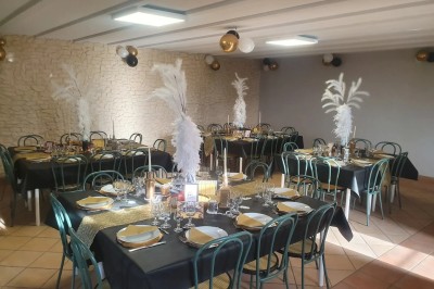 Salle décorée pour un événement, avec tables dressées, nappes noires, centres de table à plumes blanches et ballons dorés.