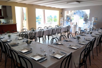 Salle décorée pour un événement, avec tables dressées, nappes noires, centres de table à plumes blanches et ballons dorés.