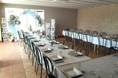 Salle décorée pour un événement, avec tables dressées, nappes noires, centres de table à plumes blanches et ballons dorés.
