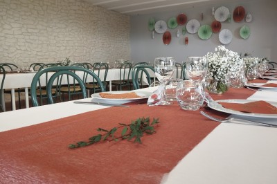 Salle décorée pour un événement, avec tables dressées, nappes noires, centres de table à plumes blanches et ballons dorés.