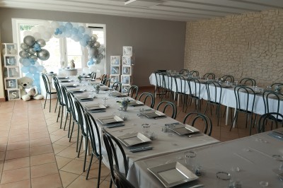 Salle décorée pour un événement, avec tables dressées, nappes noires, centres de table à plumes blanches et ballons dorés.