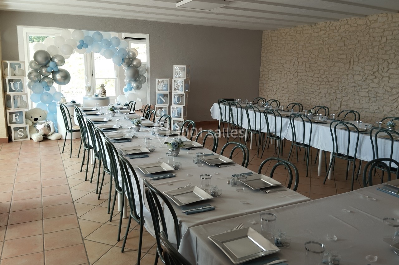 Salle décorée pour une réception avec tables dressées, ballons bleus et blancs, et cubes décoratifs près d'un ours en…