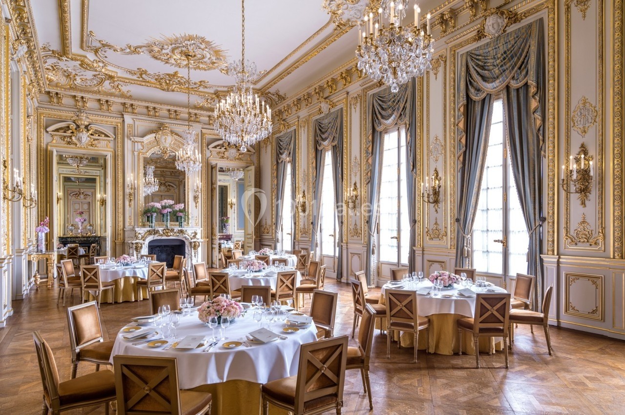 Salle de réception élégante avec décorations dorées, lustres imposants et tables rondes dressées pour un repas.
