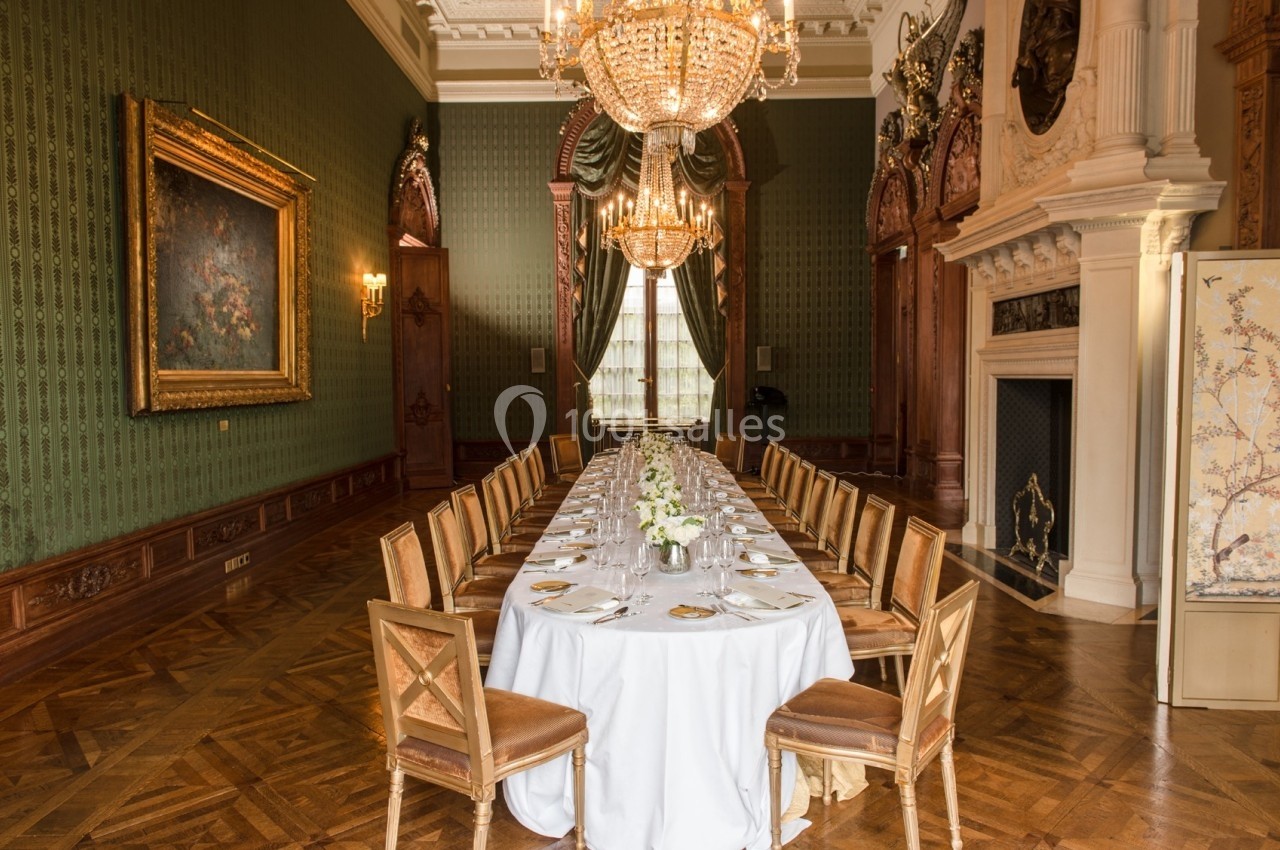 Salle à manger élégante avec une longue table dressée, chandeliers suspendus et décoration classique.