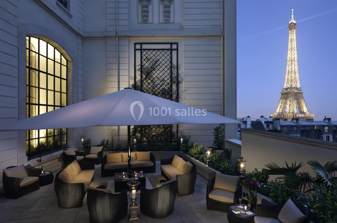 Terrasse élégante avec mobilier de jardin, éclairée le soir, offrant une vue sur la tour Eiffel illuminée.