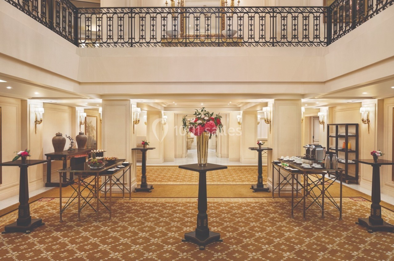 Salle élégante avec un buffet disposé sur des tables hautes, décorée de fleurs et éclairée par des appliques murales.
