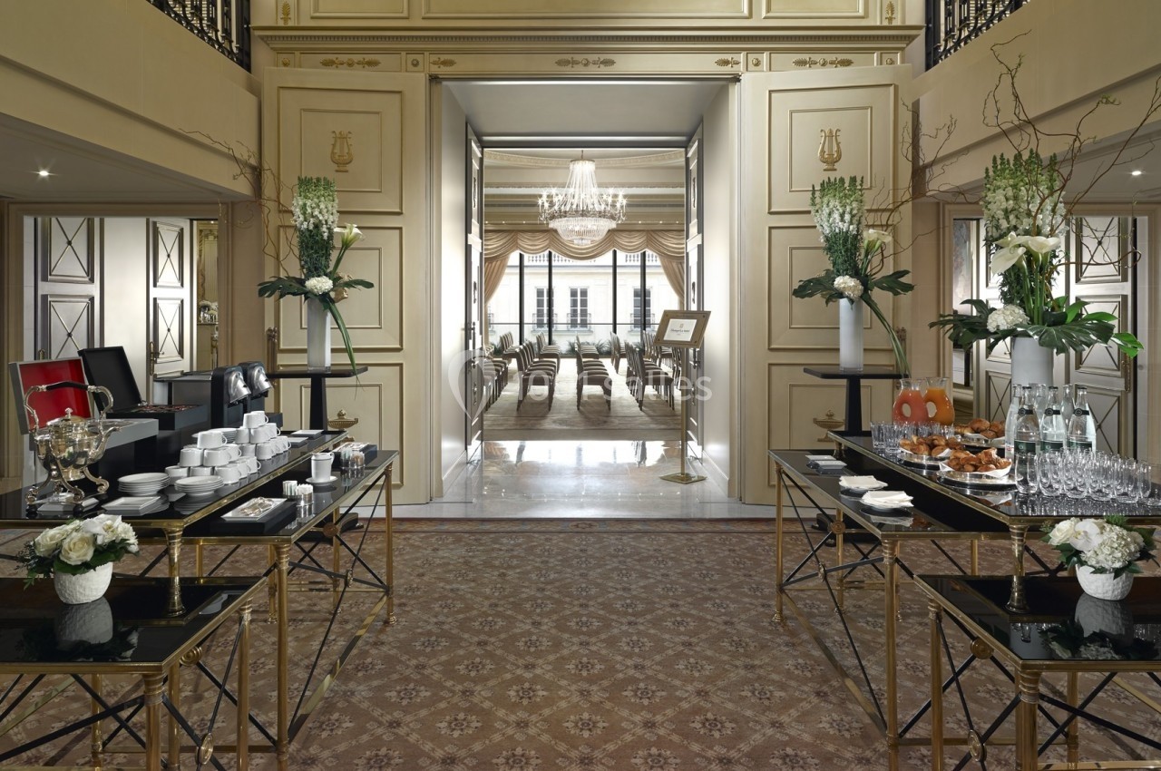 Salle élégante avec tables dressées pour un buffet, ouvrant sur une pièce lumineuse ornée d'un lustre.