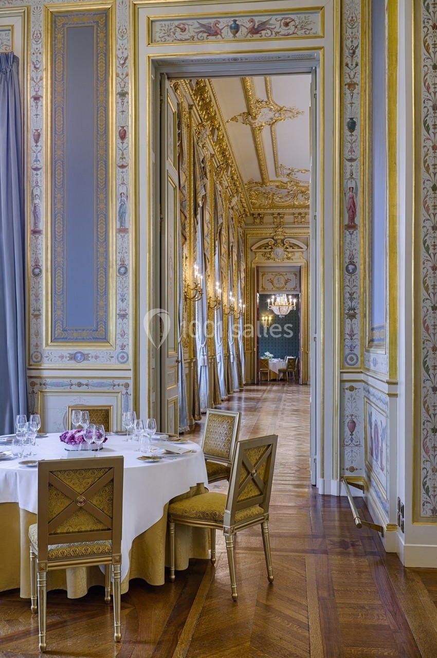 Salle élégante avec table dressée, chaises dorées et décoration intérieure ornée de moulures et fresques raffinées.