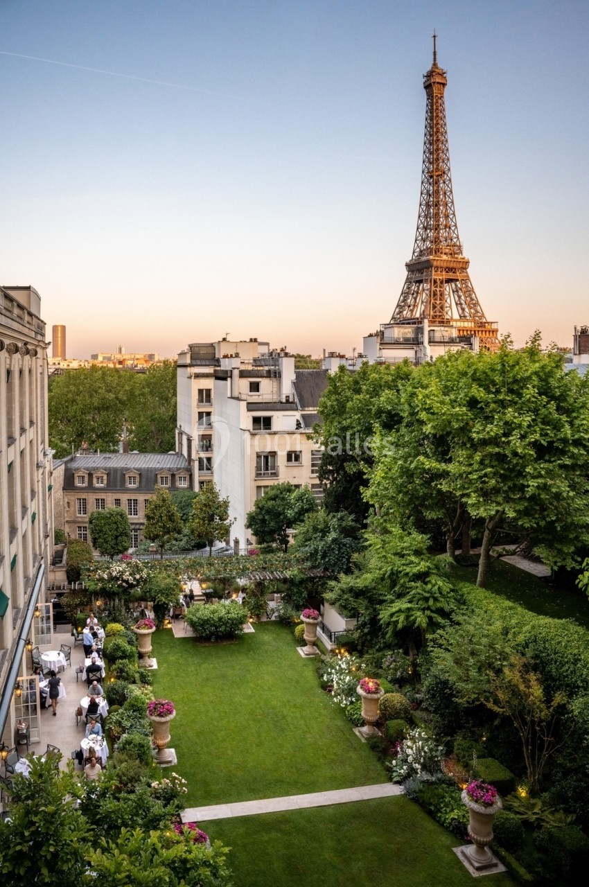 Vue sur un jardin verdoyant avec des invités et la tour Eiffel en arrière-plan au coucher du soleil.