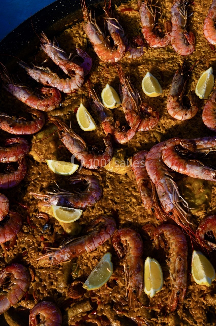 Paella garnie de crevettes roses grillées, quartiers de citron et riz doré.