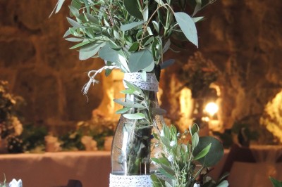 Trois bouteilles de vin posées sur un sol herbeux, entourées de fleurs blanches et jaunes.