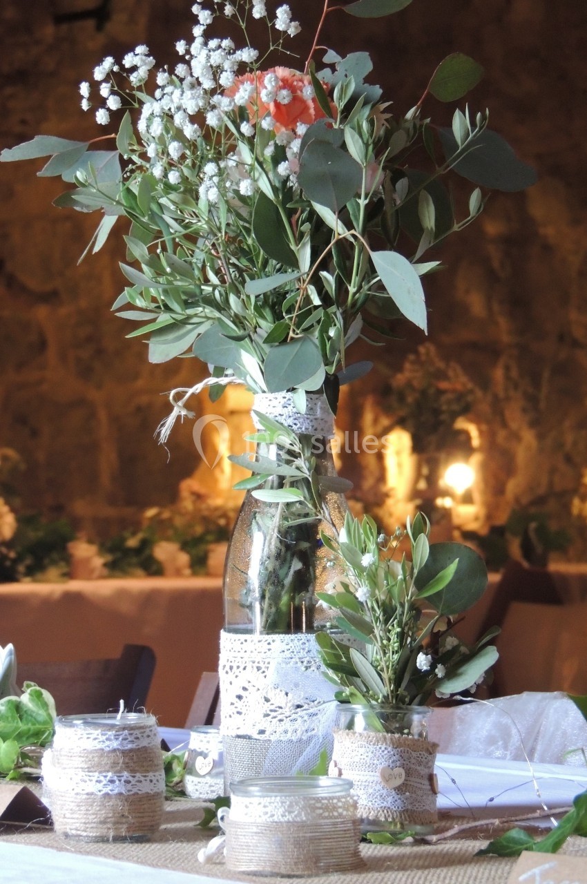 Bouquet de fleurs champêtres dans un vase décoré de dentelle, entouré de bougies et d'éléments naturels sur une table.
