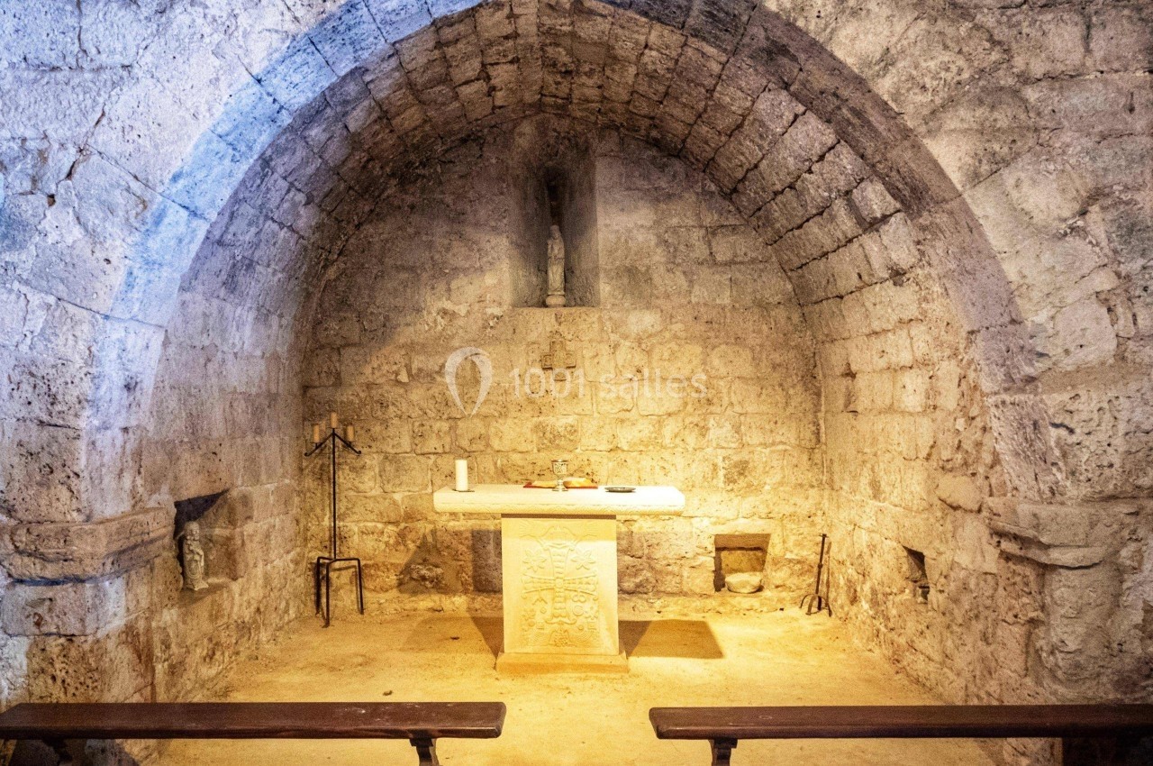 Intérieur d'une petite chapelle en pierre avec un autel central, des bancs en bois et une statue dans une alcôve.