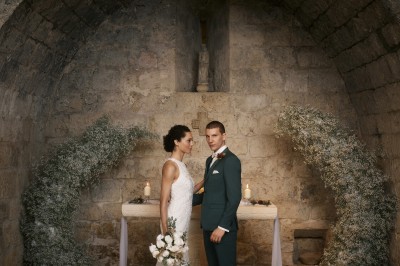 Trois bouteilles de vin posées sur un sol herbeux, entourées de fleurs blanches et jaunes.