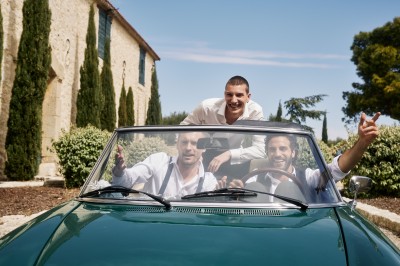 Trois bouteilles de vin posées sur un sol herbeux, entourées de fleurs blanches et jaunes.