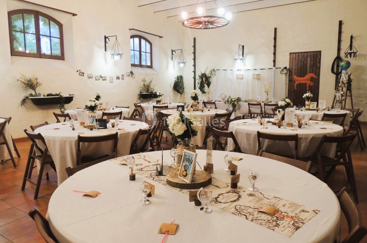 Salle de réception décorée pour un mariage, avec des tables rondes ornées de fleurs et de cartes anciennes.