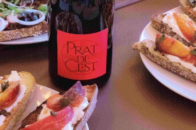 Trois bouteilles de vin posées sur un sol herbeux, entourées de fleurs blanches et jaunes.