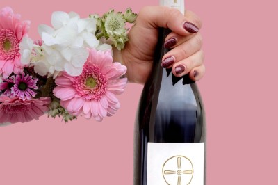 Trois bouteilles de vin posées sur un sol herbeux, entourées de fleurs blanches et jaunes.