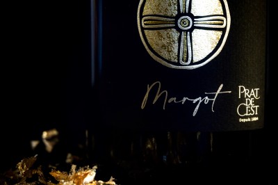 Trois bouteilles de vin posées sur un sol herbeux, entourées de fleurs blanches et jaunes.