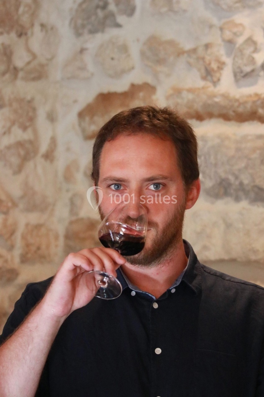Un homme déguste un verre de vin rouge devant un mur en pierre.