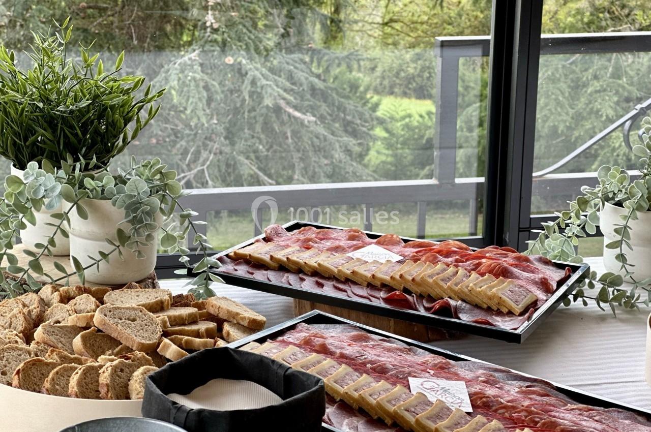 Plateaux de charcuterie et de fromage accompagnés de pain tranché, disposés sur une table près d'une baie vitrée avec vue…