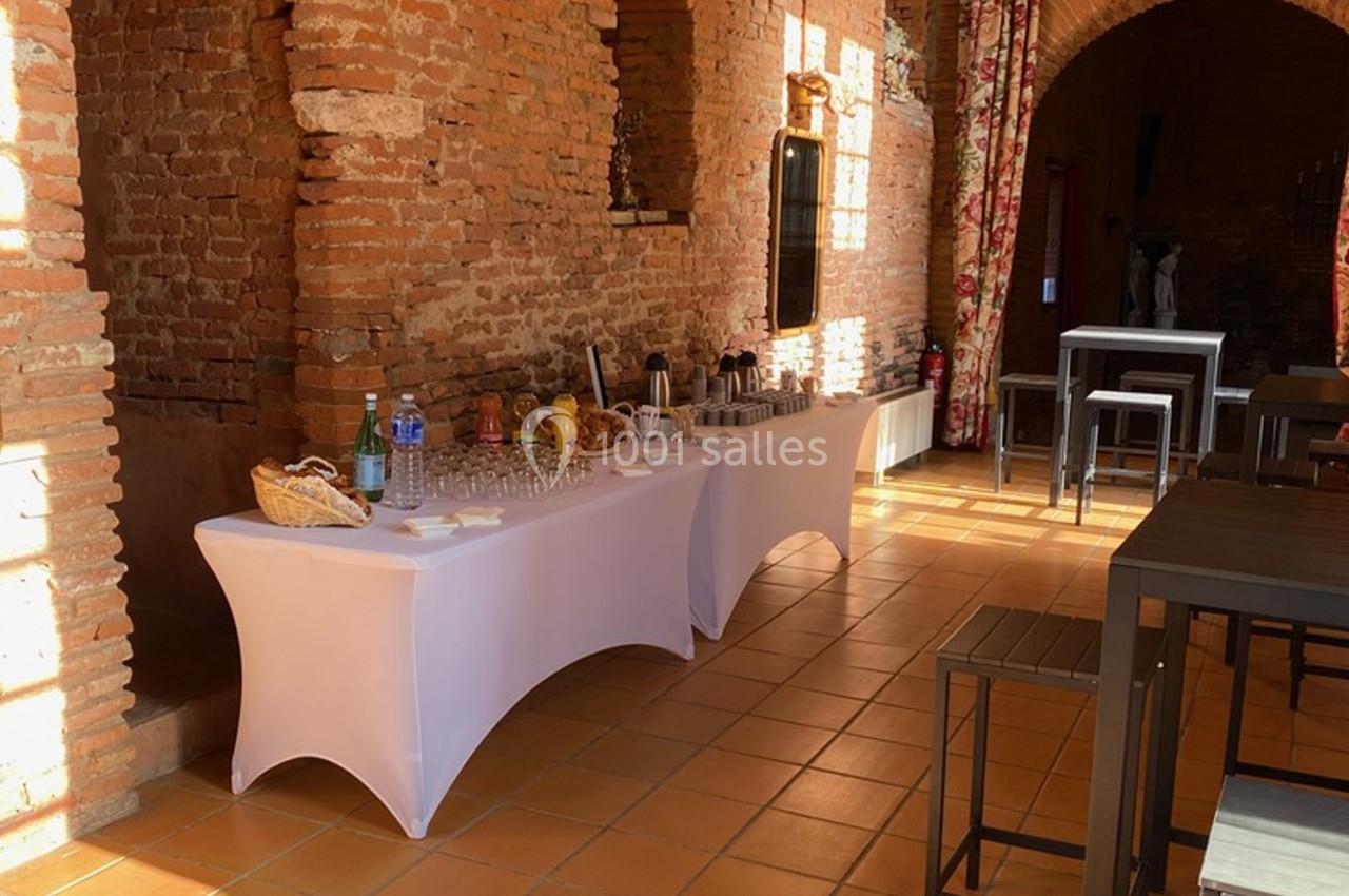 Table de buffet dressée avec boissons et verres dans une salle en briques avec lumière naturelle.