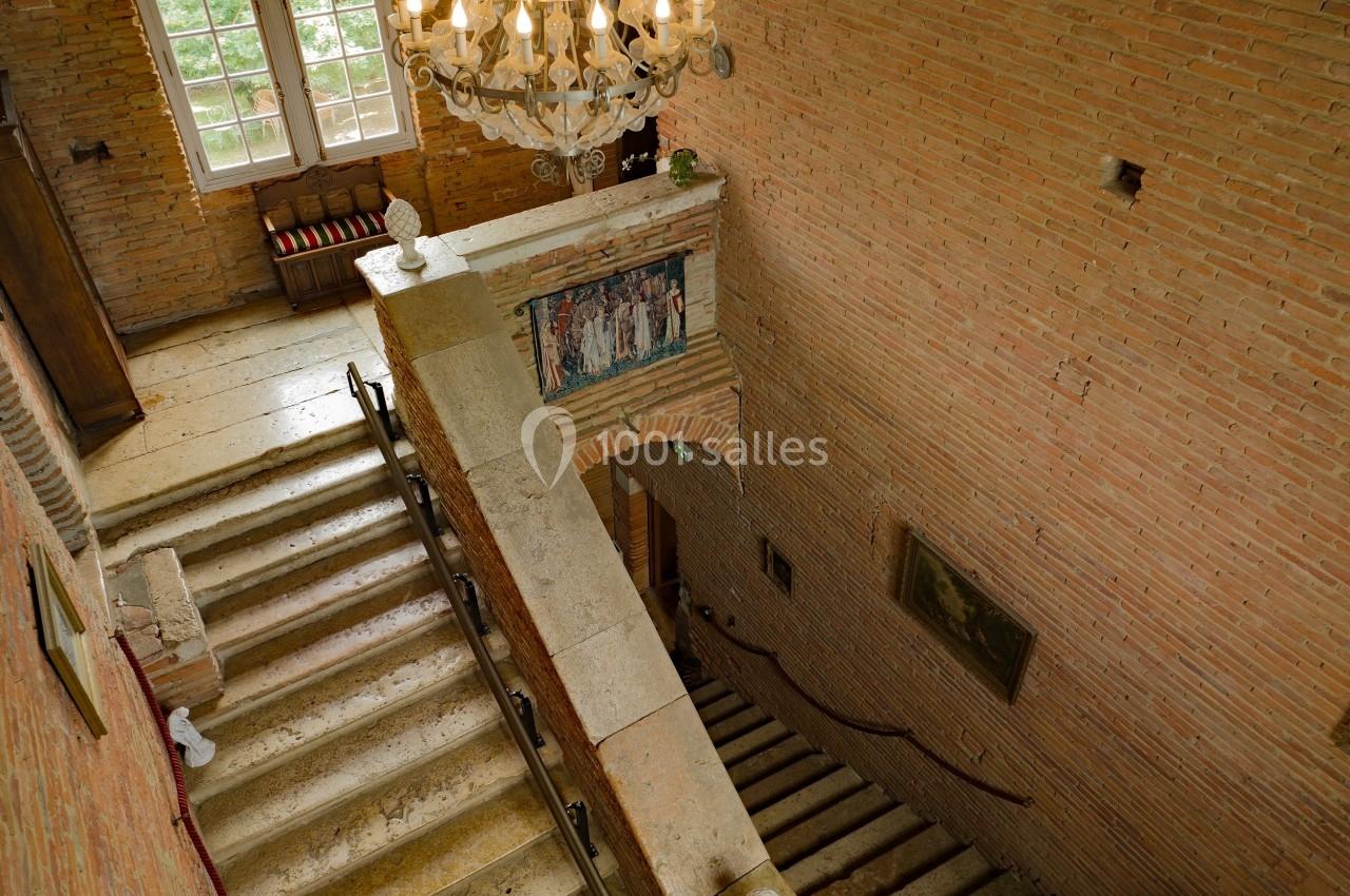 Escalier en pierre dans un bâtiment ancien avec murs en briques, lustre suspendu et lumière naturelle provenant d'une…