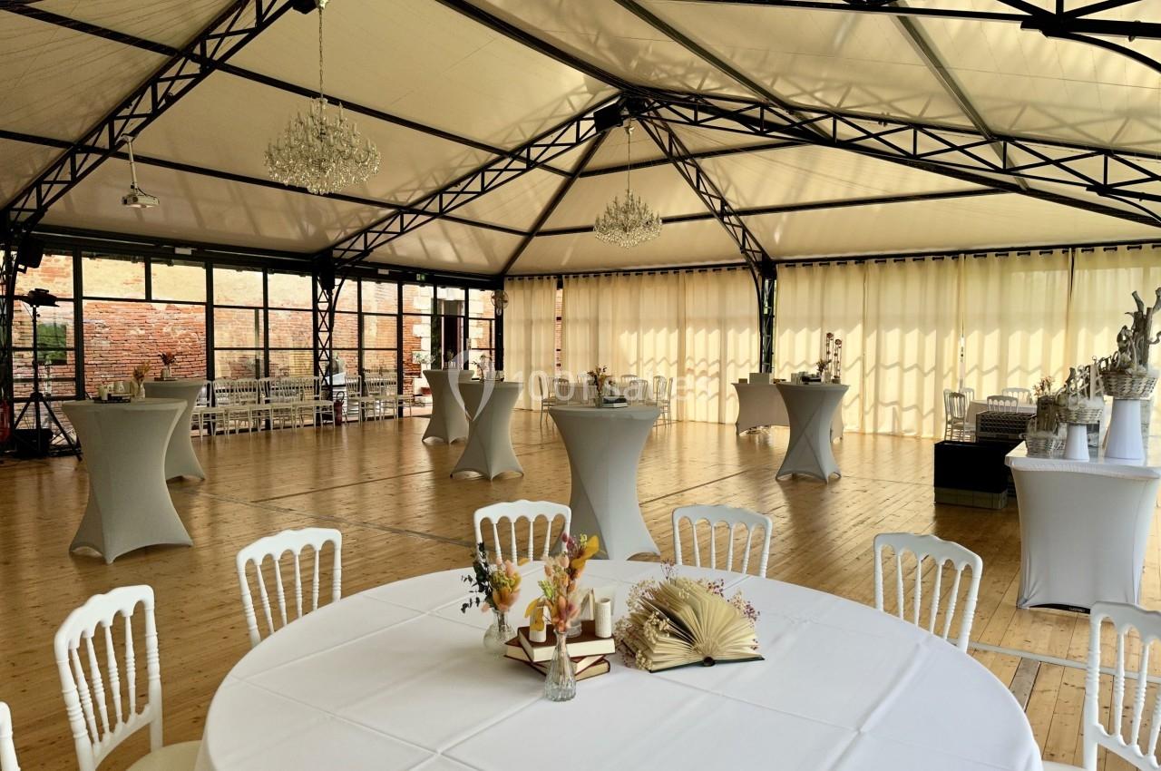 Salle de réception lumineuse avec tables rondes et mange-debout, décorée de fleurs et éclairée par des lustres.