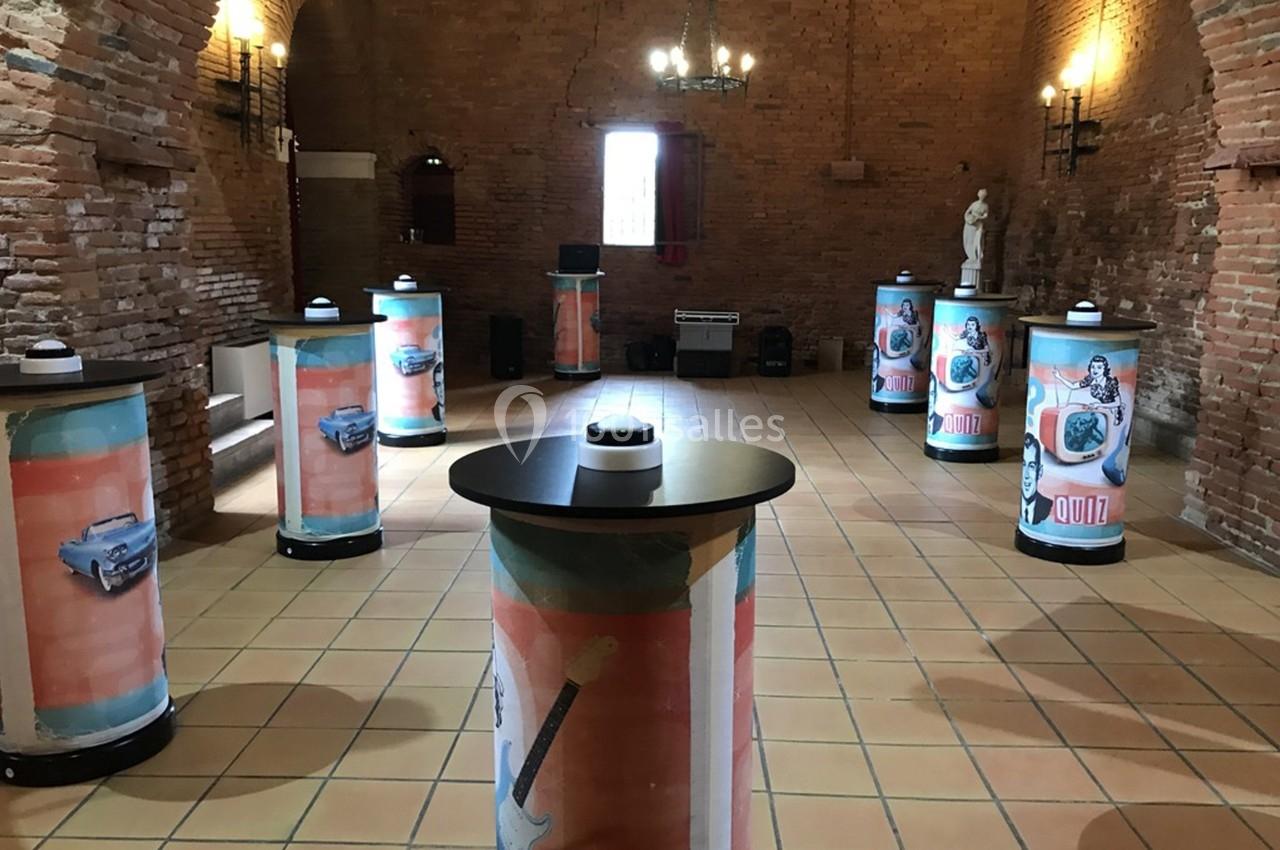 Salle en briques avec des colonnes décorées d'illustrations rétro, éclairée par des lustres et des appliques murales.