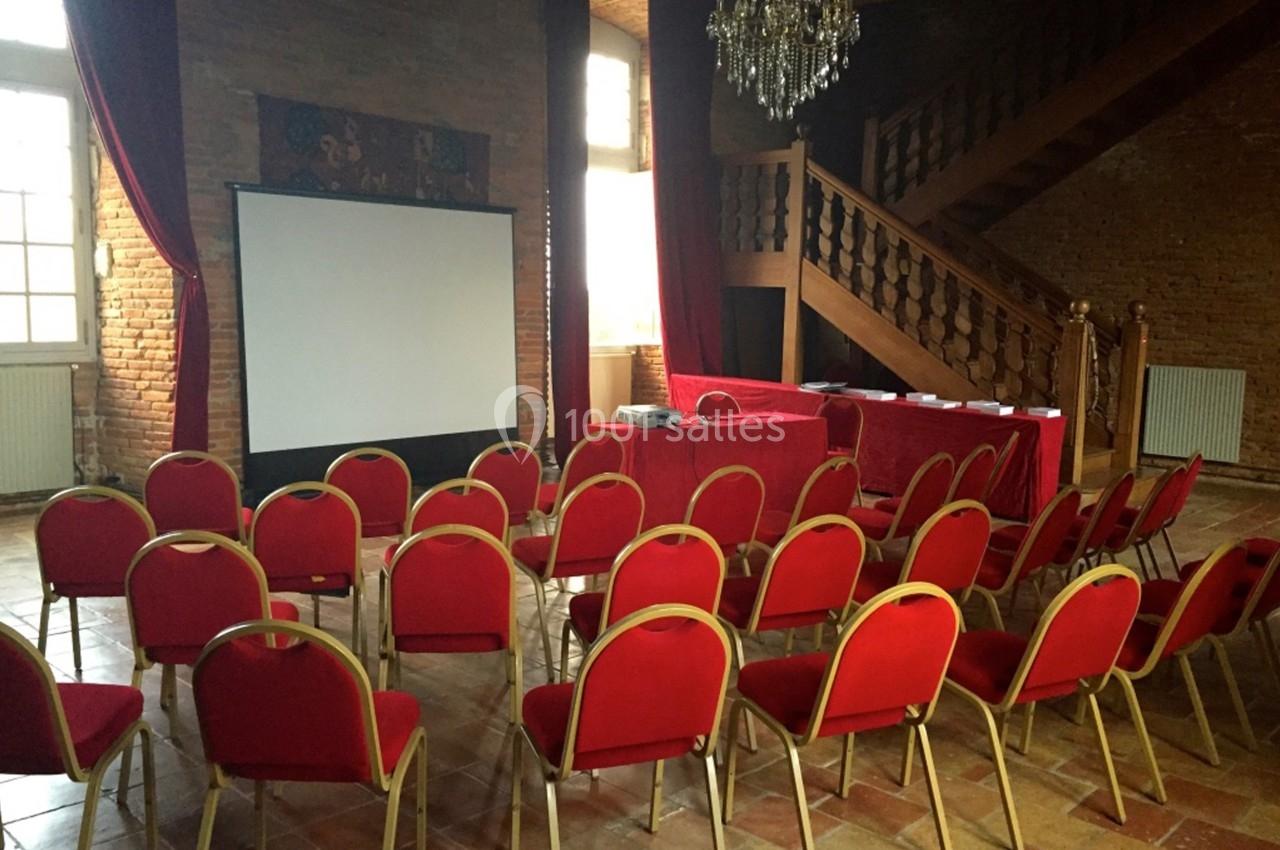Salle avec des chaises rouges alignées face à un écran de projection, dans un espace à la décoration rustique.