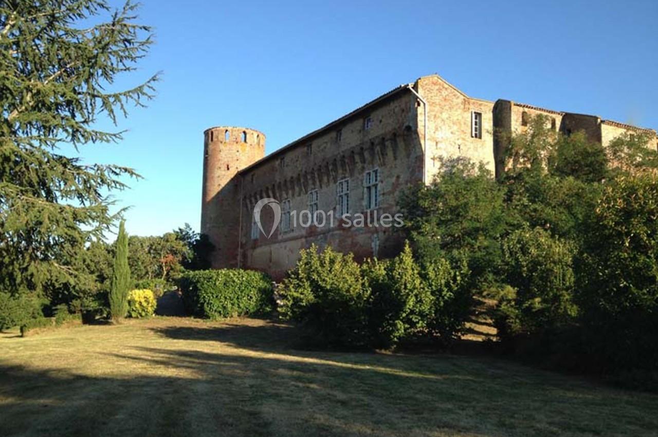 Château en pierre avec une tour ronde, entouré de verdure et baigné par une lumière en fin de journée.