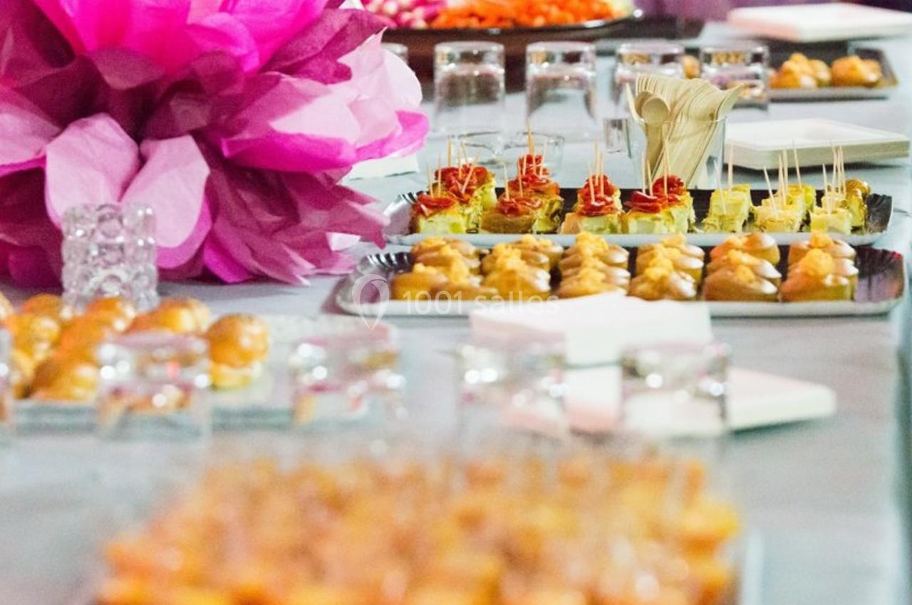 Plateau de bouchées apéritives variées disposées sur une table avec des décorations roses en arrière-plan.