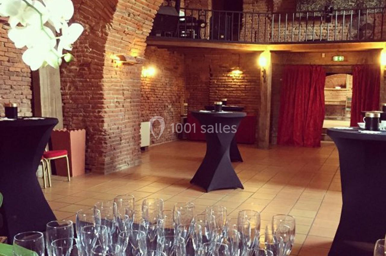 Salle en briques avec tables hautes drapées de noir, verres disposés au premier plan et mezzanine en arrière-plan.