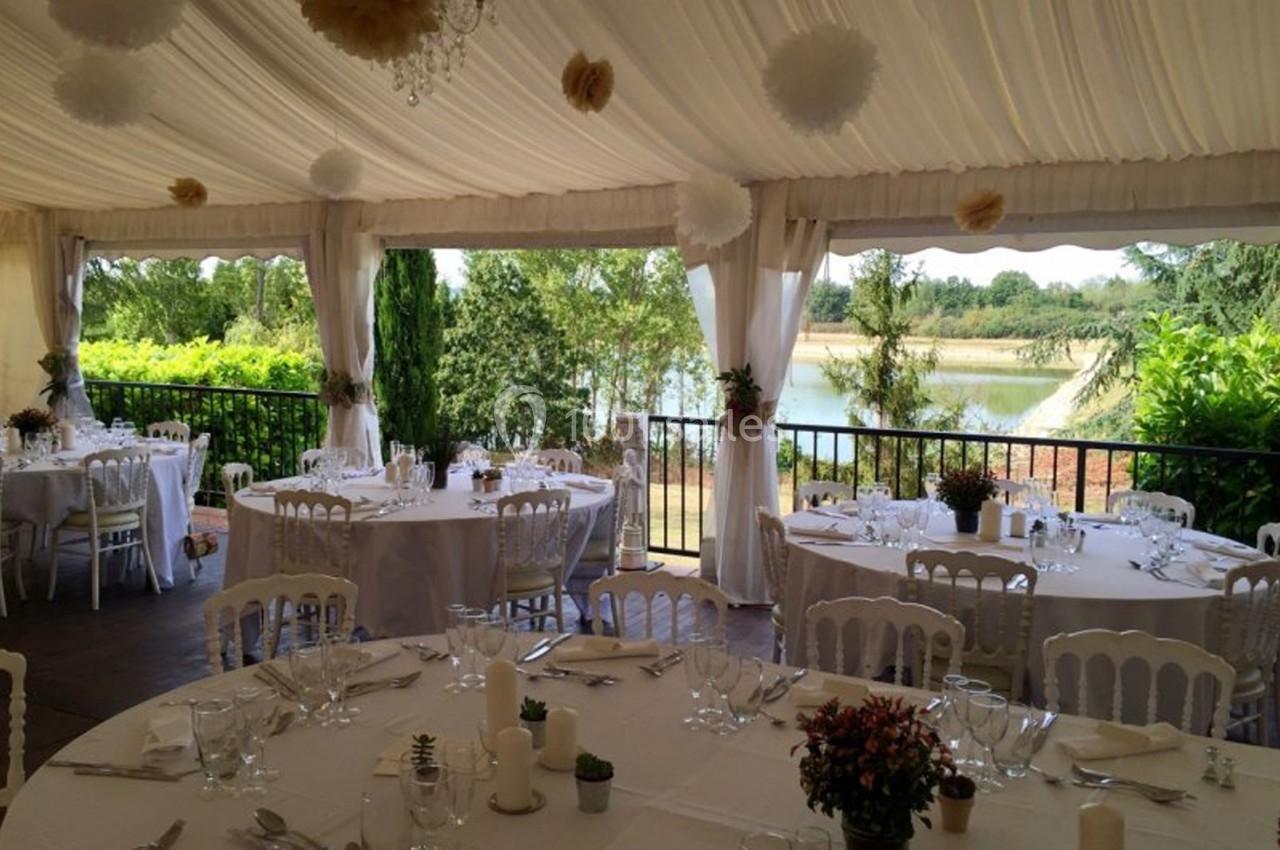 Salle de réception décorée avec des tables rondes, nappes blanches et vue sur un jardin avec un plan d'eau.