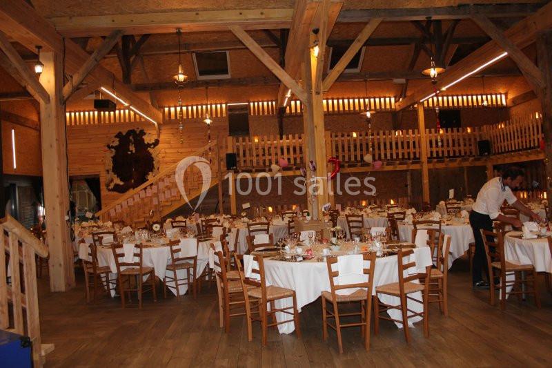 Salle de réception en bois avec tables rondes dressées, chaises en bois et décoration lumineuse chaleureuse.