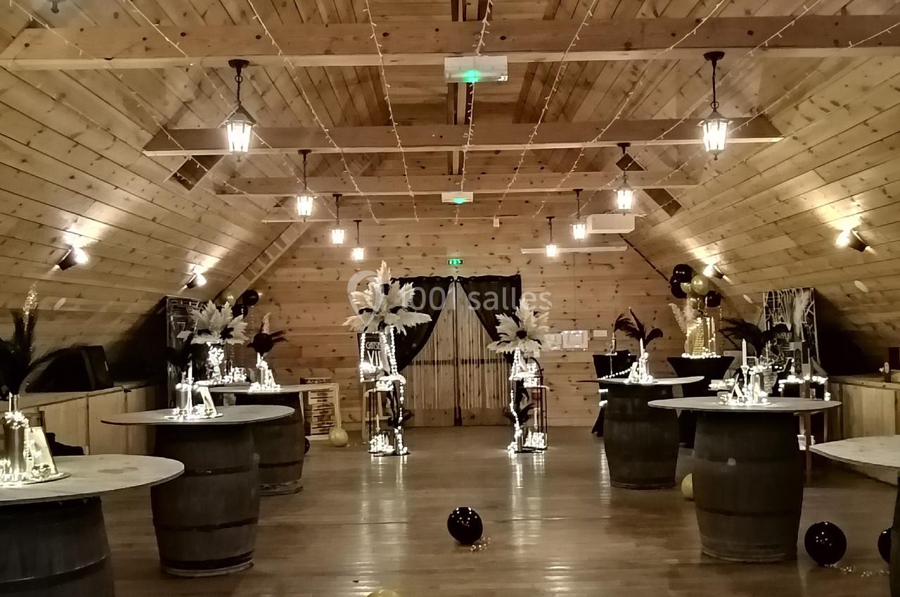 Salle en bois décorée pour un événement, avec tables sur tonneaux, ballons au sol et éclairage suspendu.