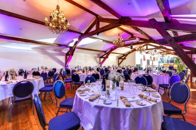 Salle vide avec sol en béton, murs en pierre et bois, tables pliées contre le mur et lustres suspendus au plafond.