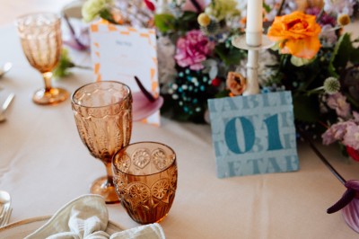 Salle vide avec sol en béton, murs en pierre et bois, tables pliées contre le mur et lustres suspendus au plafond.