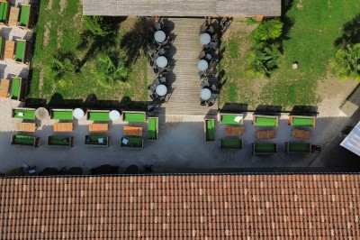 Salle vide avec sol en béton, murs en pierre et bois, tables pliées contre le mur et lustres suspendus au plafond.
